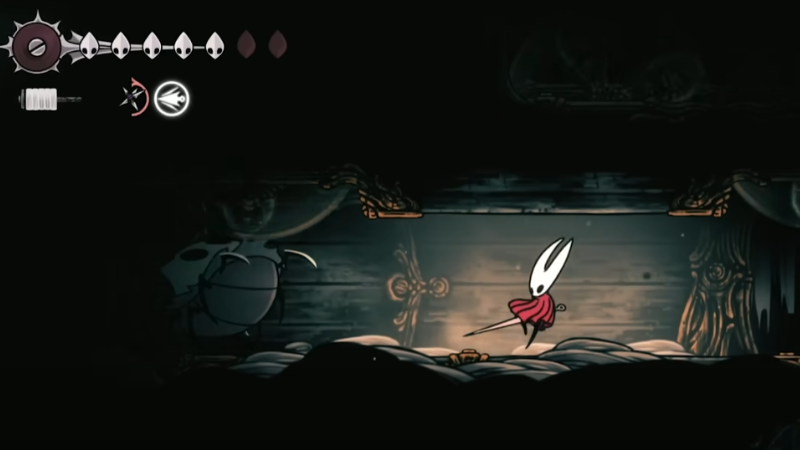 Silksong gameplay screenshot of Hornet jumping through a dim wooden room with the HUD on screen